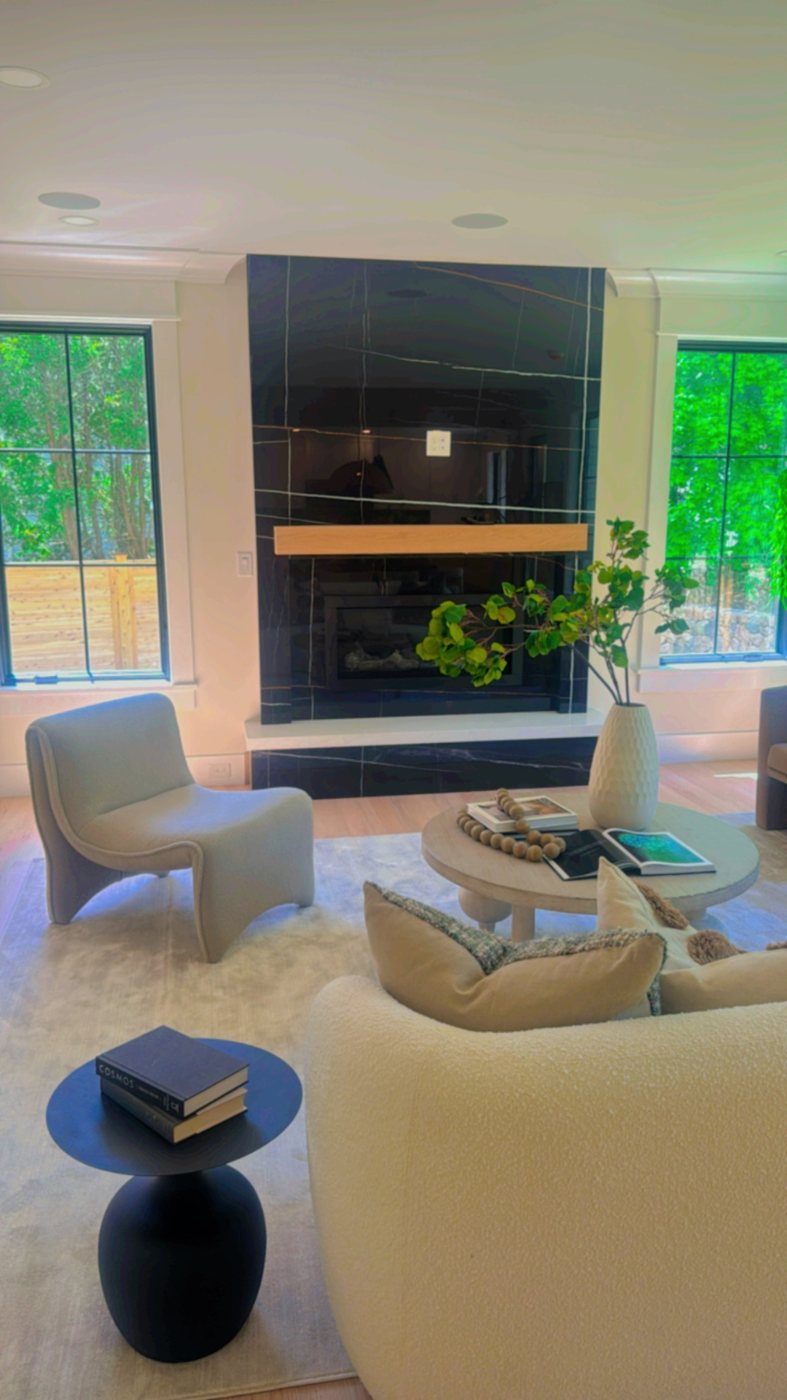 Living room fireplace wall clad in Laurent Noir stone with gold and white veining, oak mantel and white stone hearth