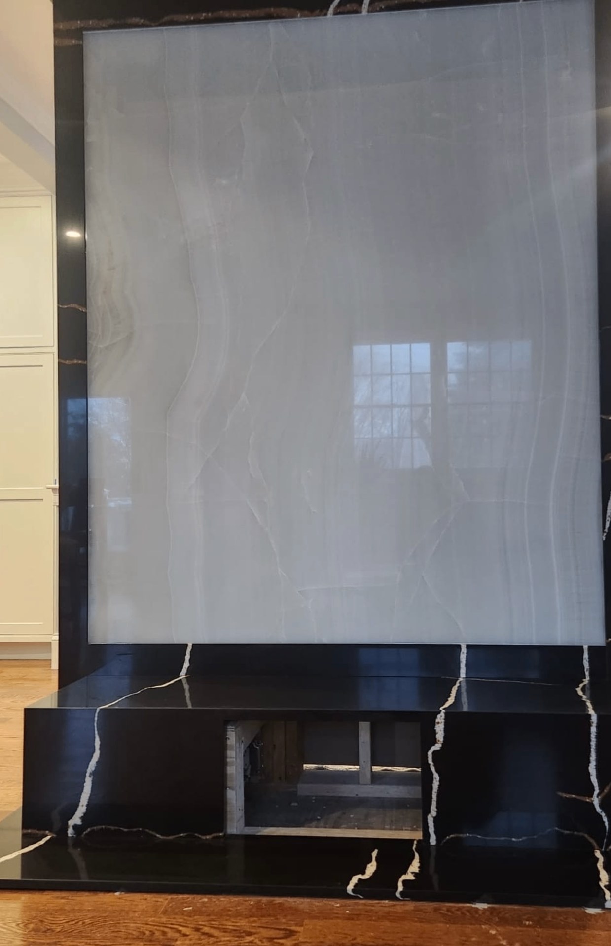 Floor-to-ceiling black stone fireplace wall with gold and white veining framing a large light onyx panel