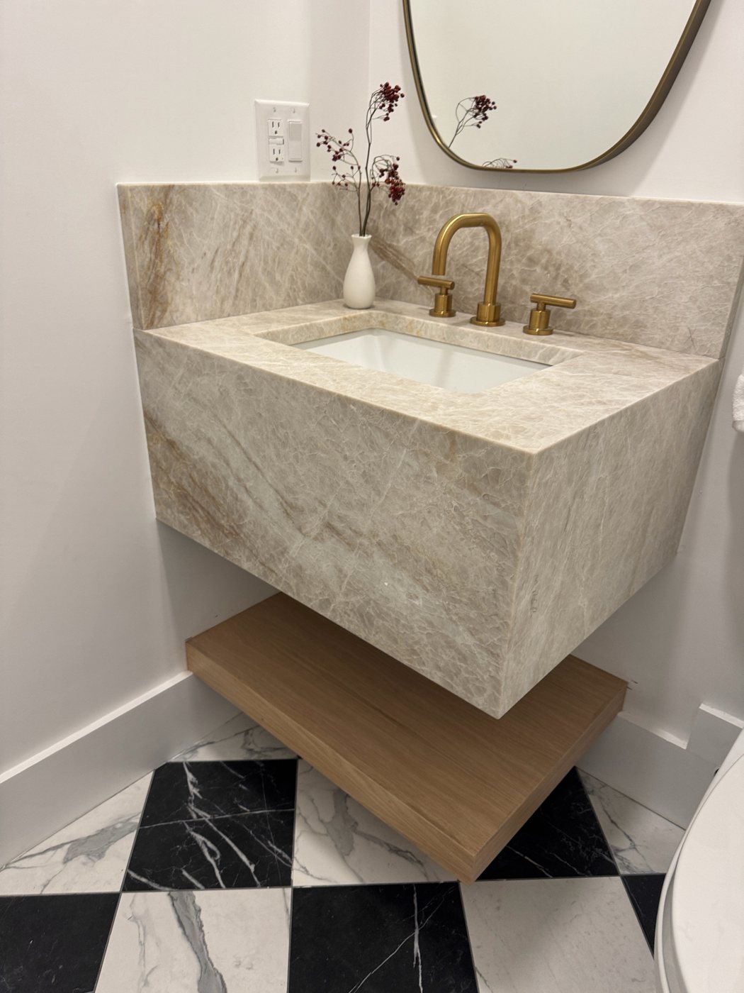 Floating bathroom vanity wrapped in Cristallo stone with a matching backsplash, brass faucet and oak shelf below