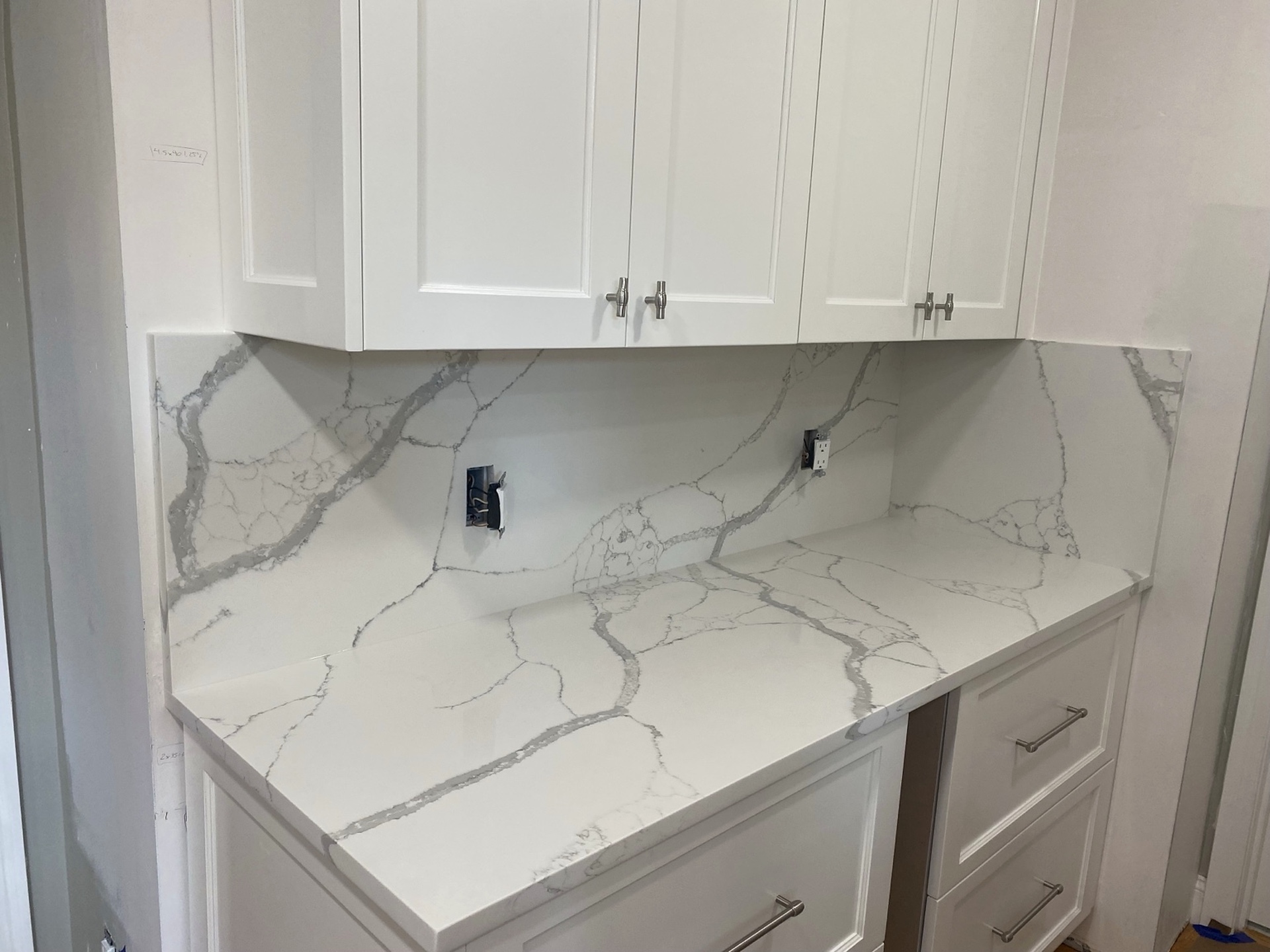 White cabinetry with a veined stone countertop and matching full-height backsplash