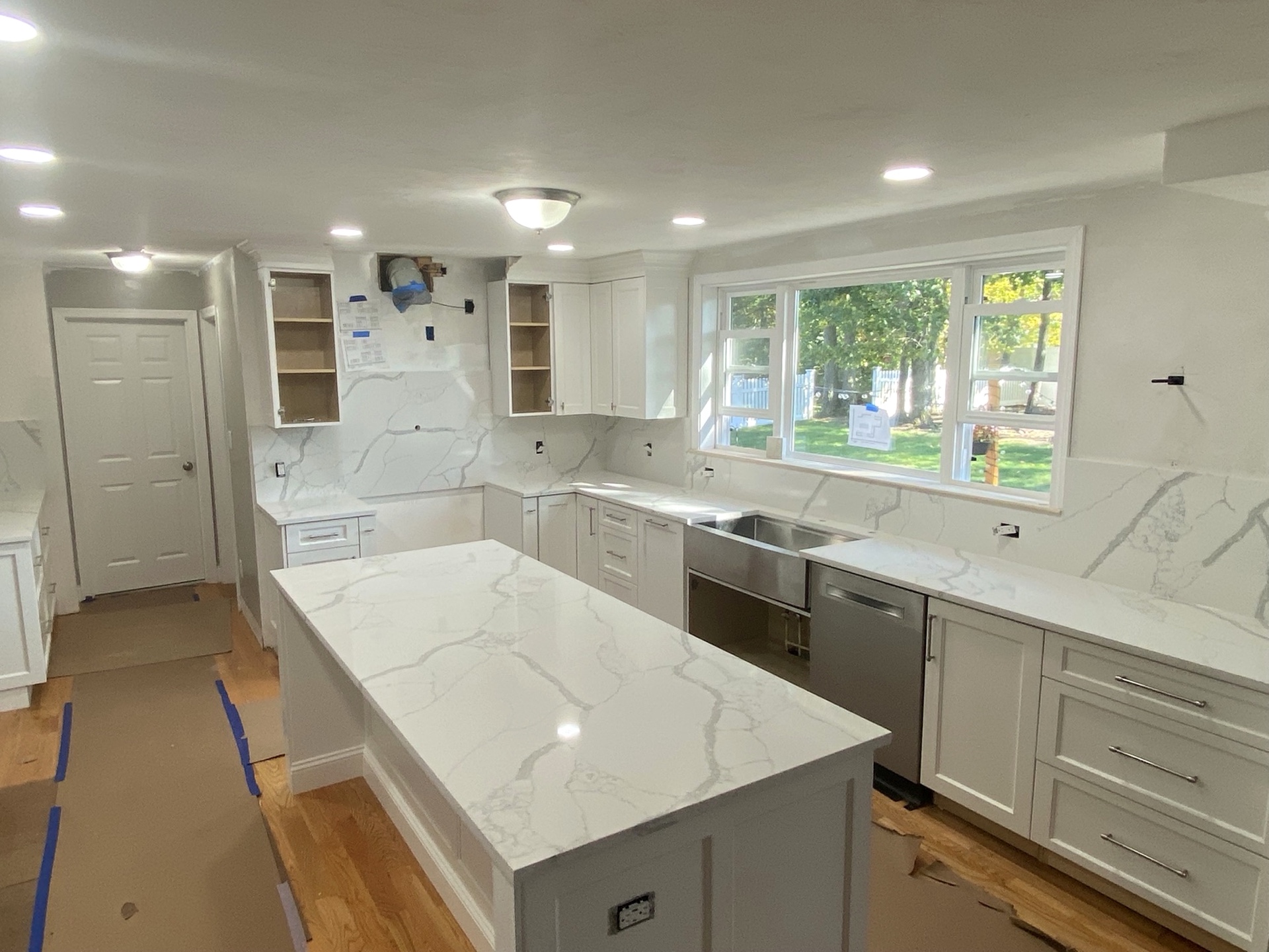 White kitchen with a large veined stone island, perimeter countertops and full-height backsplash