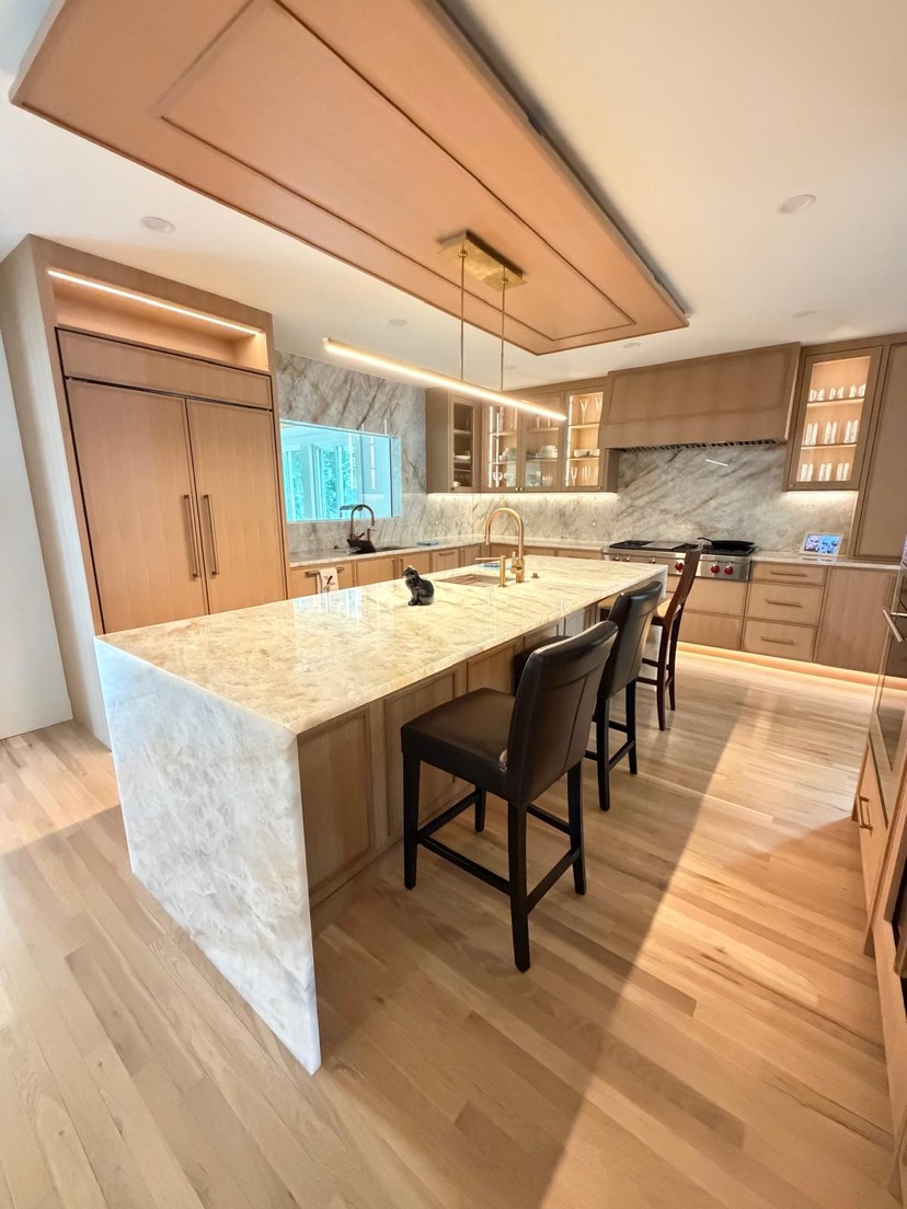 Waterfall stone island with a matching full-height backsplash in a light-oak kitchen