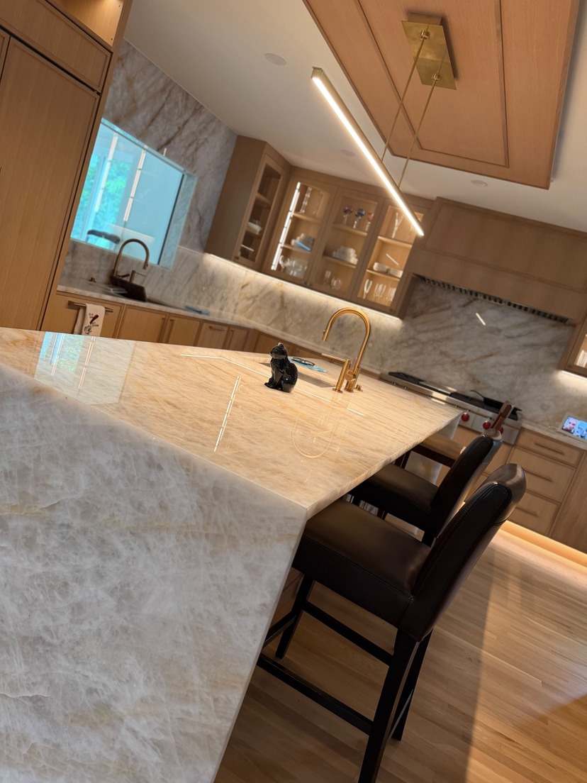 Polished stone countertop and full-height stone backsplash in a warm oak kitchen