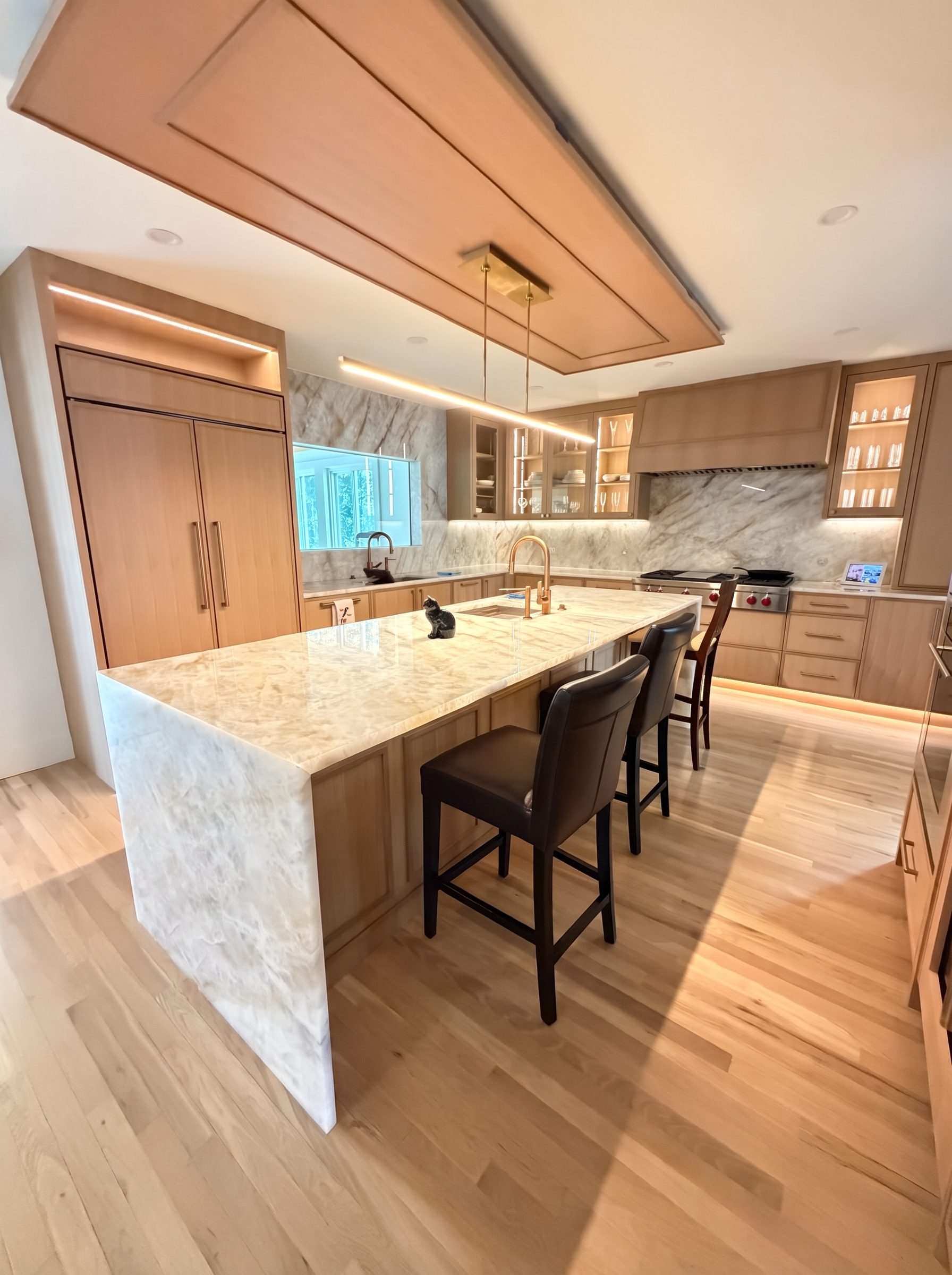 Quartzite waterfall island in a warm white-oak kitchen by Authentic Marble & Granite