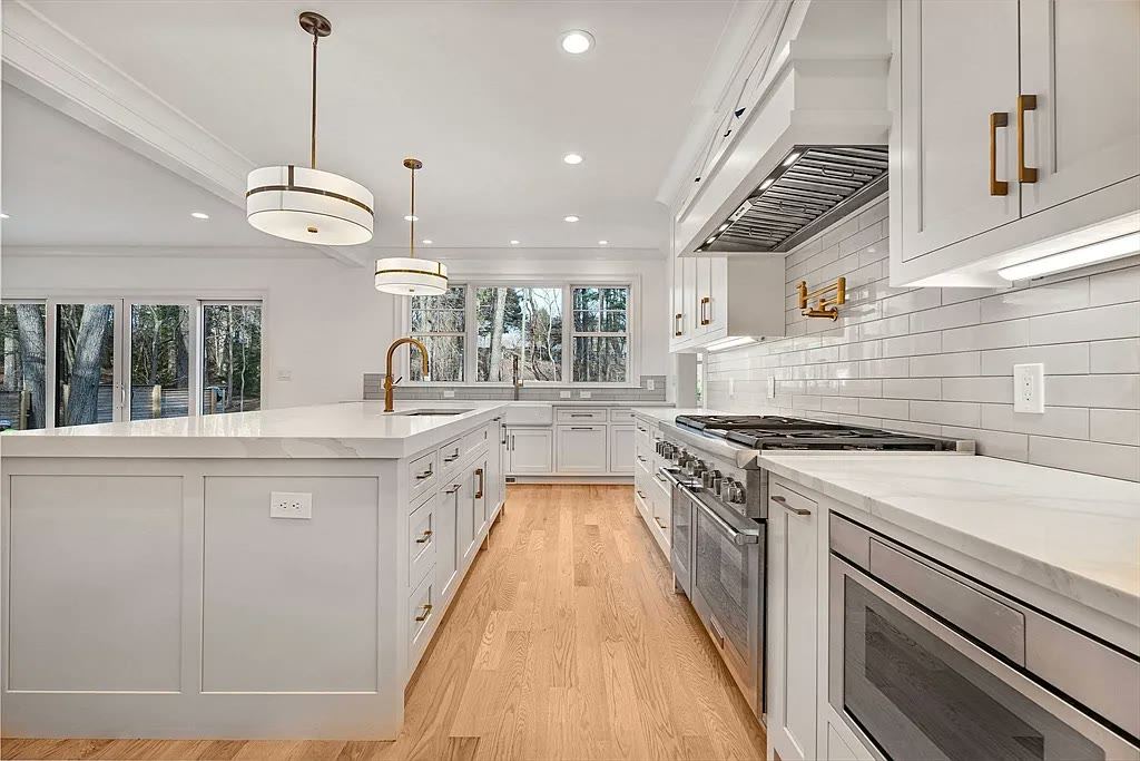 Long white kitchen with stone countertops, subway backsplash and brass fixtures
