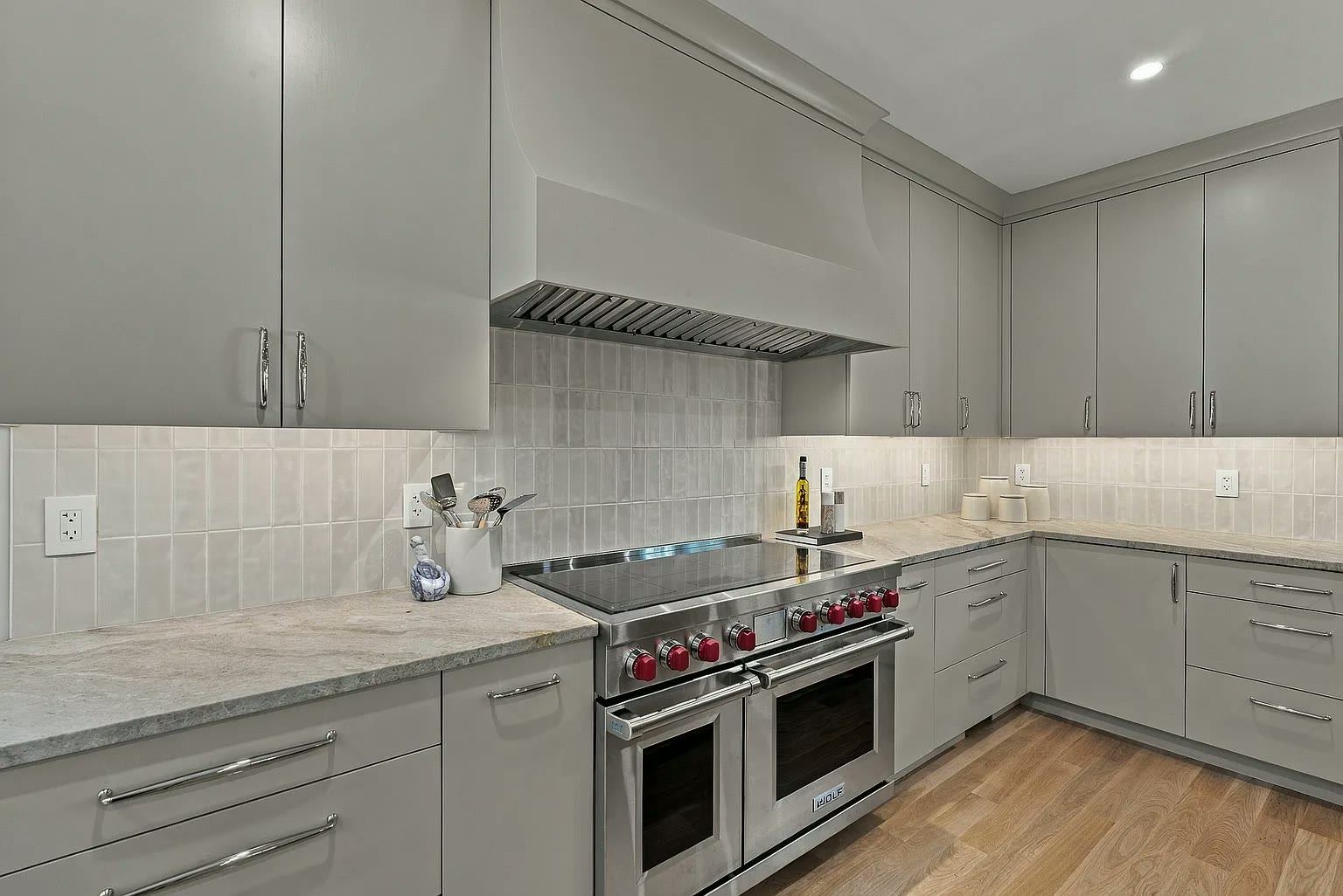 Grey kitchen with a light tiled backsplash, professional range and stone counters