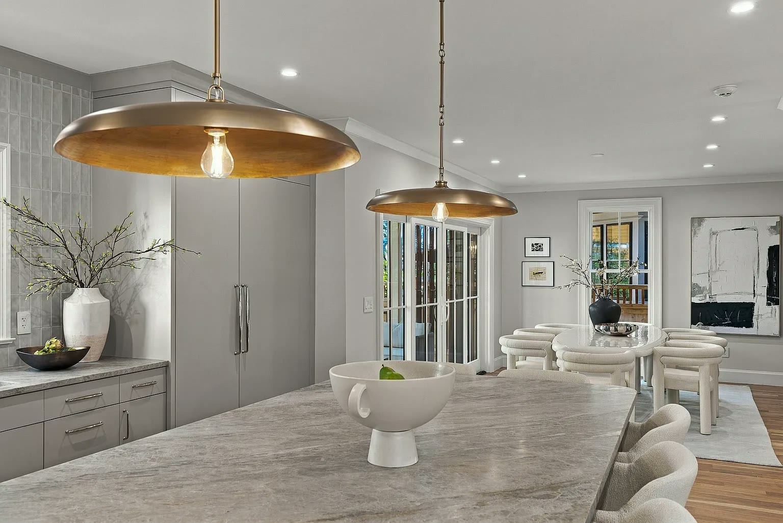 Stone kitchen island lit by bronze pendant lights with a dining area beyond